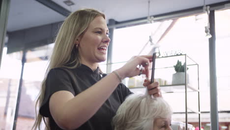 Senior-Woman-Having-Hair-Cut-By-Female-Stylist-In-Hairdressing-Salon