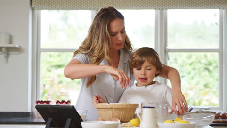 Mother-And-Son-In-Pyjamas-Baking-In-Kitchen-At-Home-Following-Recipe-On-Digital-Tablet