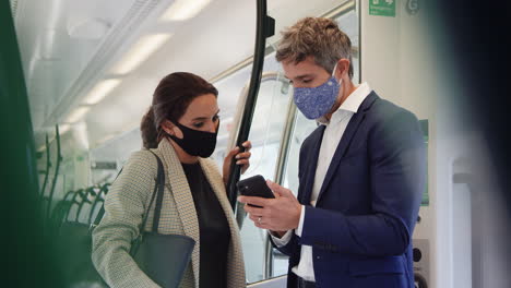 Geschäftspendler-Stehen-Während-Der-Pandemie-Mit-Mobiltelefonen-Im-Zugwaggon-Und-Tragen-PSA-Gesichtsmasken