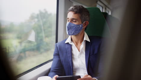 Geschäftsmann-Im-Zug-Mit-Mobiltelefon-Und-PSA-Gesichtsmaske-Während-Einer-Gesundheitspandemie