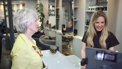 Senior-Woman-Making-Contactless-Payment-To-Stylist-In-Salon-With-Credit-Card