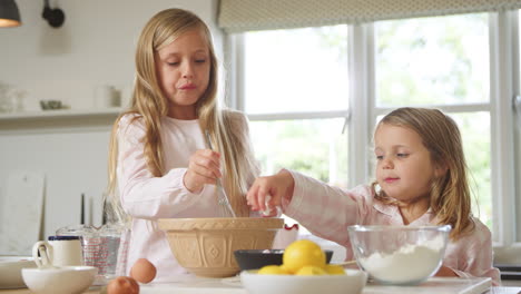 Two-Girls-Wearing-Pyjamas-Baking-In-Kitchen-At-Home-Together