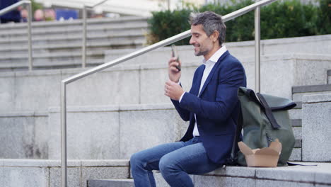 Businessman-Sitting-Outside-On-Lunch-Break-Talking-On-Mobile-Phone