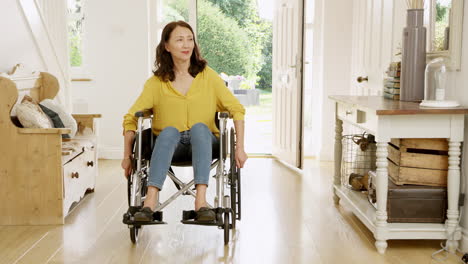 Mature-Asian-woman-in-wheelchair-pushing-himself-in-hallway-at-home-towards-camera--shot-in-slow-motion