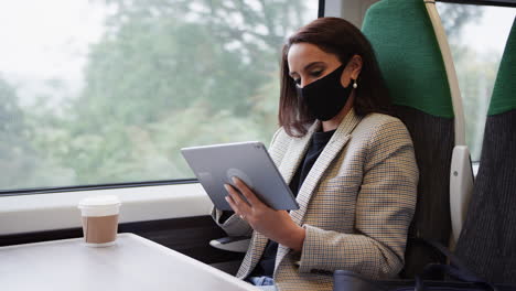 Businesswoman-On-Train-Using-Digital-Tablet-Wearing-PPE-Face-Mask-During-Health-Pandemic