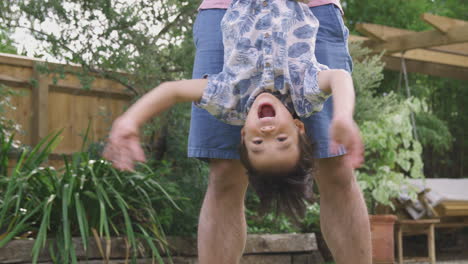 Asian-Father-Holding-Son-Upside-Down-By-Legs-In-Garden-As-They-Play-Game-Together