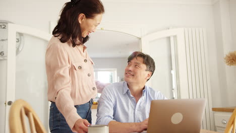 Mature-Asian-woman-bringing-husband-coffee-at-home-as-they-check-household-bills-on-laptop-together--shot-in-slow-motion