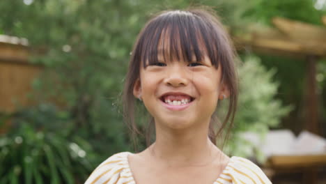 Retrato-De-Una-Chica-Asiática-Sonriente-A-La-Que-Le-Faltan-Dientes-Delanteros-Divirtiéndose-En-El-Jardín-De-Casa
