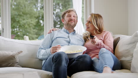 Ein-Paar-Beim-Date-Abend-Sitzt-Zu-Hause-Auf-Dem-Sofa,-Lacht-Und-Schaut-Sich-Mit-Popcorn-Einen-Film-Im-Fernsehen-An