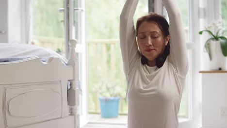 Reife-Asiatische-Frau-Im-Schlafanzug-Sitzt-Auf-Dem-Boden-Des-Schlafzimmers-Und-Meditiert-In-Yoga-Pose-–-Aufgenommen-In-Zeitlupe