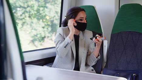 Geschäftsfrau-Im-Zug-Schminkt-Sich,-Während-Sie-Während-Einer-Gesundheitspandemie-Eine-PSA-Gesichtsmaske-Trägt