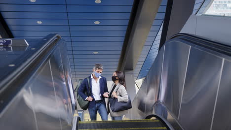 Geschäftsmann-Und-Geschäftsfrau-Fahren-Rolltreppe-Am-Bahnhof-Und-Tragen-Bei-Einer-Pandemie-Eine-PSA-Gesichtsmaske