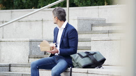 Businessman-Sitting-Outside-On-Lunch-Break-Eating-Takeaway-Meal-From-Sustainable-Recyclable-Carton