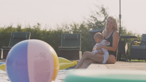 Mother-With-Baby-Daughter-Having-Fun-On-Summer-Vacation--Sitting-By-Outdoor-Swimming-Pool