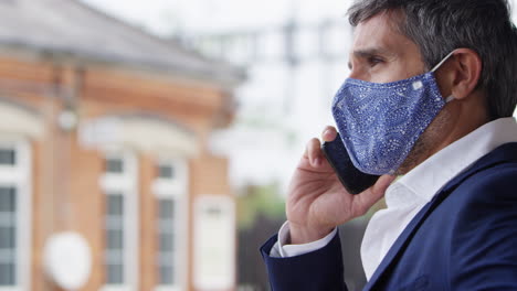 Businessman-On-Railway-Platform-Talking-On-Mobile-Phone-Wearing-PPE-Face-Mask-During-Health-Pandemic