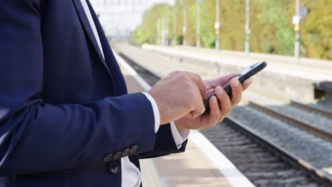 Close-Up-Of-Businessman-Standing-On-Railway-Platform-Using-Mobile-Phone