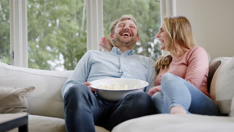 Couple-On-Date-Night-Sitting-On-Sofa-At-Home-Laughing-And-Watching-Movie-On-TV-With-Popcorn
