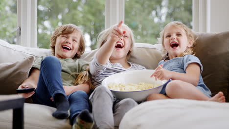 Drei-Kinder-Sitzen-Zu-Hause-Auf-Dem-Sofa,-Lachen-Und-Schauen-Mit-Popcorn-Fern