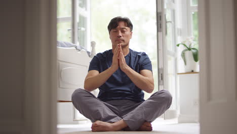 Mature-Asian-man-in-pyjamas-sitting-on-bedroom-floor-stretching-and-meditating-in-yoga-pose---shot-in-slow-motion