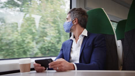 Hombre-De-Negocios-En-Tren-Usando-Un-Teléfono-Móvil-Usando-Máscara-Facial-Ppe-Durante-Una-Pandemia-De-Salud