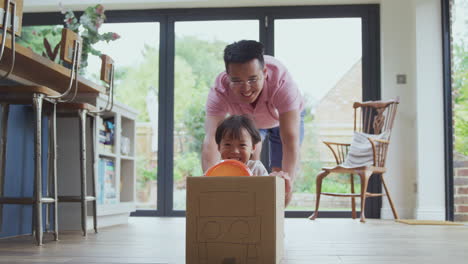 Asian-Father-And-Son-Pushing-Son-Around-Kitchen-Floor-At-Home-In-Junk-Modelled-Car