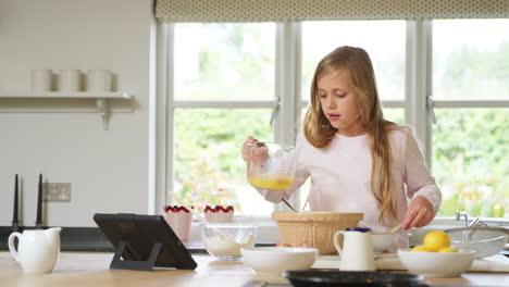 Girl-Wearing-Pyjamas-Baking-In-Kitchen-At-Home-Following-Recipe-On-Digital-Tablet