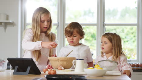 Kinder-Im-Schlafanzug-Backen-In-Der-Heimischen-Küche-Pfannkuchen-Nach-Einem-Rezept-Auf-Einem-Digitalen-Tablet