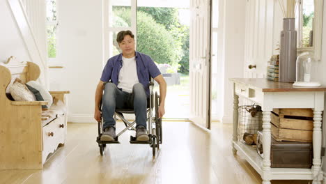 Mature-Asian-man-in-wheelchair-pushing-himself-in-hallway-at-home-towards-camera--shot-in-slow-motion