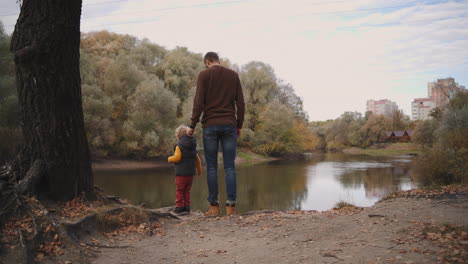 man-with-his-little-son-are-admiring-beauty-of-forest-lake-at-autumn-day-travelling-and-resting-at-nature-at-fall-back-view-of-father-and-child