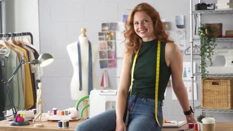 Portrait-Of-Female-Student-Or-Business-Owner-With-Tape-Measure-Working-In-Fashion-Sitting-On-Desk