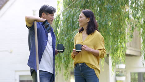 Mature-Asian-couple-taking-a-break-from-tidying-leaves-in-garden-chatting-whilst-drinking-hot-drink---shot-in-slow-motion
