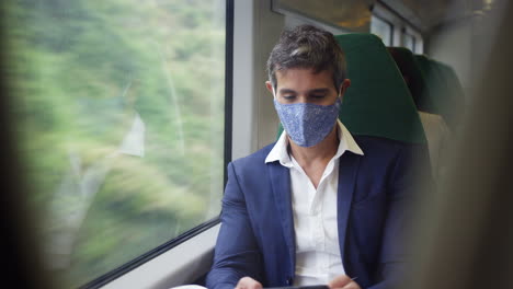 Hombre-De-Negocios-En-Tren-Usando-Un-Teléfono-Móvil-Usando-Máscara-Facial-Ppe-Durante-Una-Pandemia-De-Salud