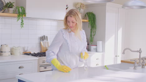 Panning-shot-of-woman-at-home-in-kitchen-wearing-rubber-gloves-cleaning-down-work-surface-using-cleaning-spray---shot-in-slow-motion