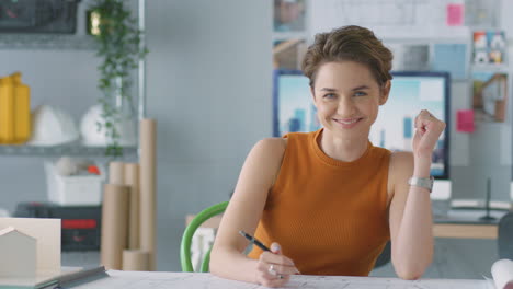 Portrait-Of-Smiling-Female-Architect-In-Office-Working-At-Desk-With-Model-Of-Building