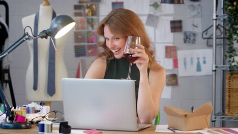 Female-Owner-Of-Fashion-Business-With-Glass-of-Wine-Making-Video-Call-On-Laptop-In-Studio