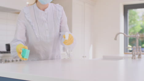 Woman-in-face-mask-at-home-in-kitchen-wearing-rubber-gloves-cleaning-down-work-surface-using-cleaning-spray-during-health-pandemic----shot-in-slow-motion
