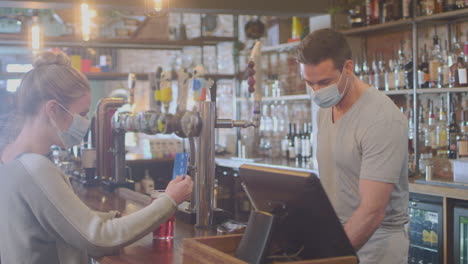 Female-Customer-Wearing-Mask-In-Bar-Making-Contactless-Payment-For-Drinks-During-Health-Pandemic