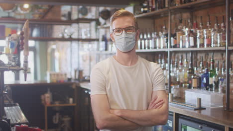 Portrait-Of-Male-Bar-Worker-Wearing-Face-Mask-During-Health-Pandemic-Standing-Behind-Counter