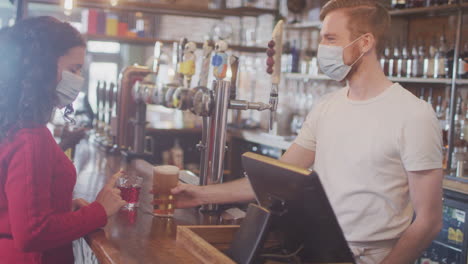 Female-Customer-Wearing-Mask-In-Bar-Making-Contactless-Payment-For-Drinks-During-Health-Pandemic