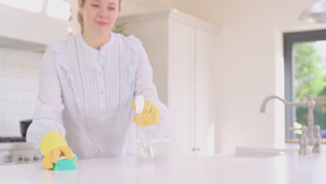 Frau-Zu-Hause-In-Der-Küche,-Die-Gummihandschuhe-Trägt-Und-Die-Arbeitsfläche-Mit-Reinigungsspray-Reinigt-–-Aufgenommen-In-Zeitlupe