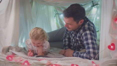 Father-and-young-daughter-with-colouring-book-in-homemade-camp-in-child's-bedroom-at-home---shot-in-slow-motion