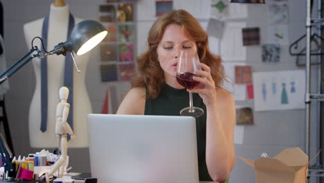 Female-Owner-Of-Fashion-Business-With-Glass-of-Wine-Working-Late-On-Laptop-In-Studio