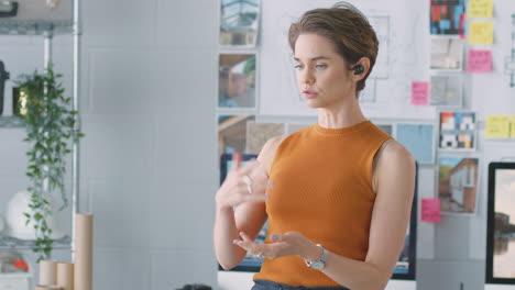 Female-Architect-Standing-In-Office-Talking-To-Client-Using-Wireless-Earphones