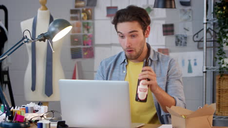 Male-Owner-Of-Fashion-Business-With-Bottle-Of-Beer-Making-Video-Call-On-Laptop-In-Studio