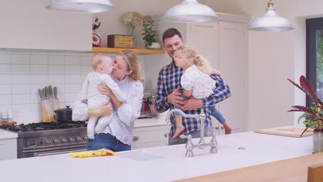 Family-in-kitchen-with-parents-holding-children-after-doing-household-chores---shot-in-slow-motion