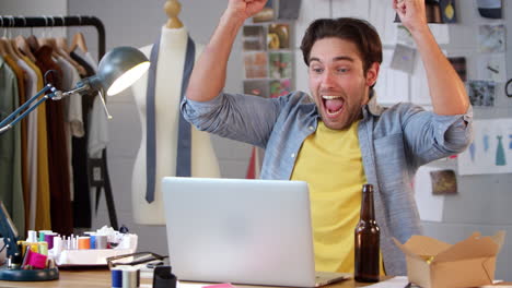 Male-Fashion-Designer-With-Bottle-Of-Beer-Watching-Sport-On-Laptop-And-Celebrating-In-Studio