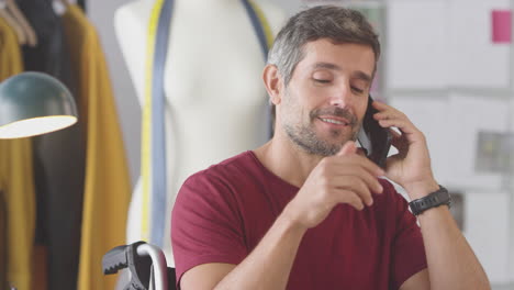 Mature-Male-Fashion-Designer-In-Wheelchair-In-Studio-Talking-On-Mobile-Phone