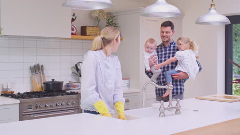 Father-carrying-daughter-and-baby-son-to-see-mother-as-she-washes-dishes-in-sink---shot-in-slow-motion