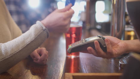 Close-Up-Of-Female-Customer-In-Bar-Making-Contactless-Payment-For-Drinks-In-Health-Pandemic