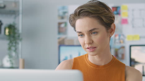Close-Up-Of-Smiling-Female-Architect-In-Office-Working-At-Desk-On-Laptop